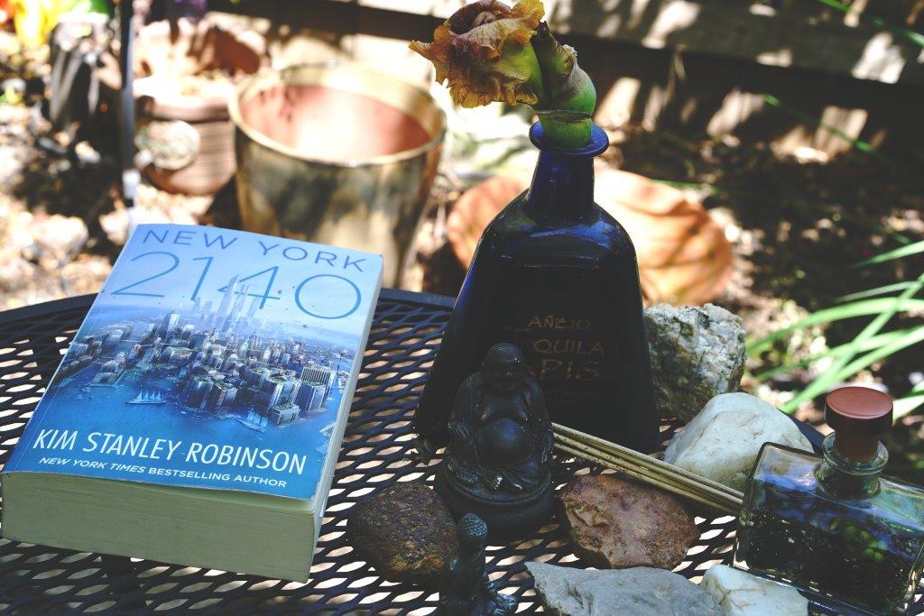 Das Bild zeigt den Arbeitstisch von Kim stanley Robinson in seinem Garten. Auf dem Tisch gibt es eine Buddhafigur, Räucherstäbchen und Steine